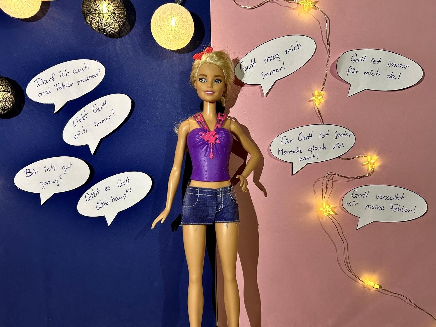 Darstellung einer Barbie, die vor einem 2farbigen HIntergrund liegt - auf einer Seite der Barbie sind Sprechblasen mit existenziellen und religiösen Fragen, auf der anderen Seite, kann man mögliche Antworten zu diesen Fragen lesen.