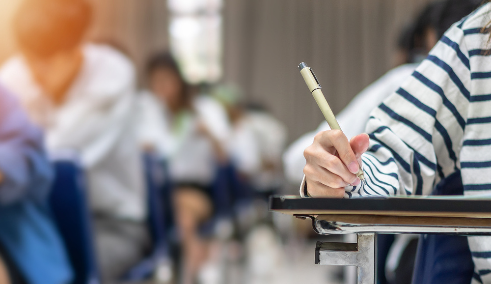 Exam at school with student's taking educational admission test in class, thinking hard, writing answer in university classroom, education and world literacy day concept